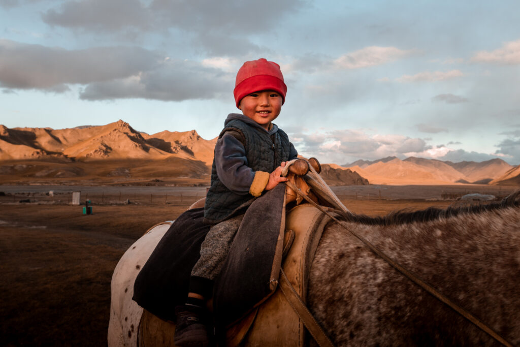Local Kyrgyz child learning how to ride a horse at yurt camp in Kok-Kiya valley, Kyrgyzstan