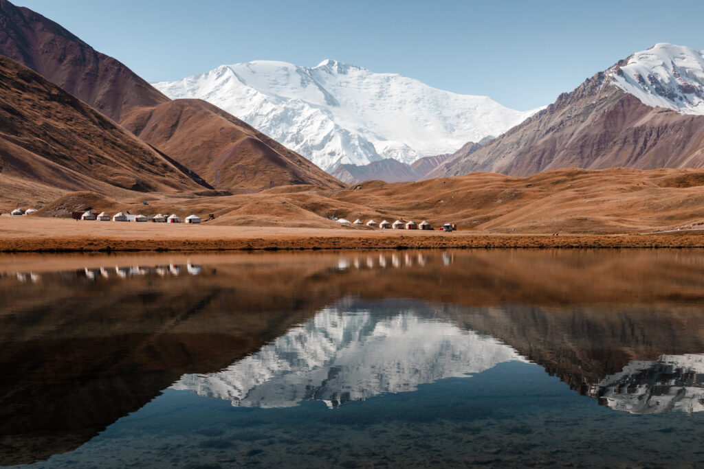 Yurt camps and Lenin Peak reflected in Tupar-Kul in the Pamir mountains, Kyrgyzstan